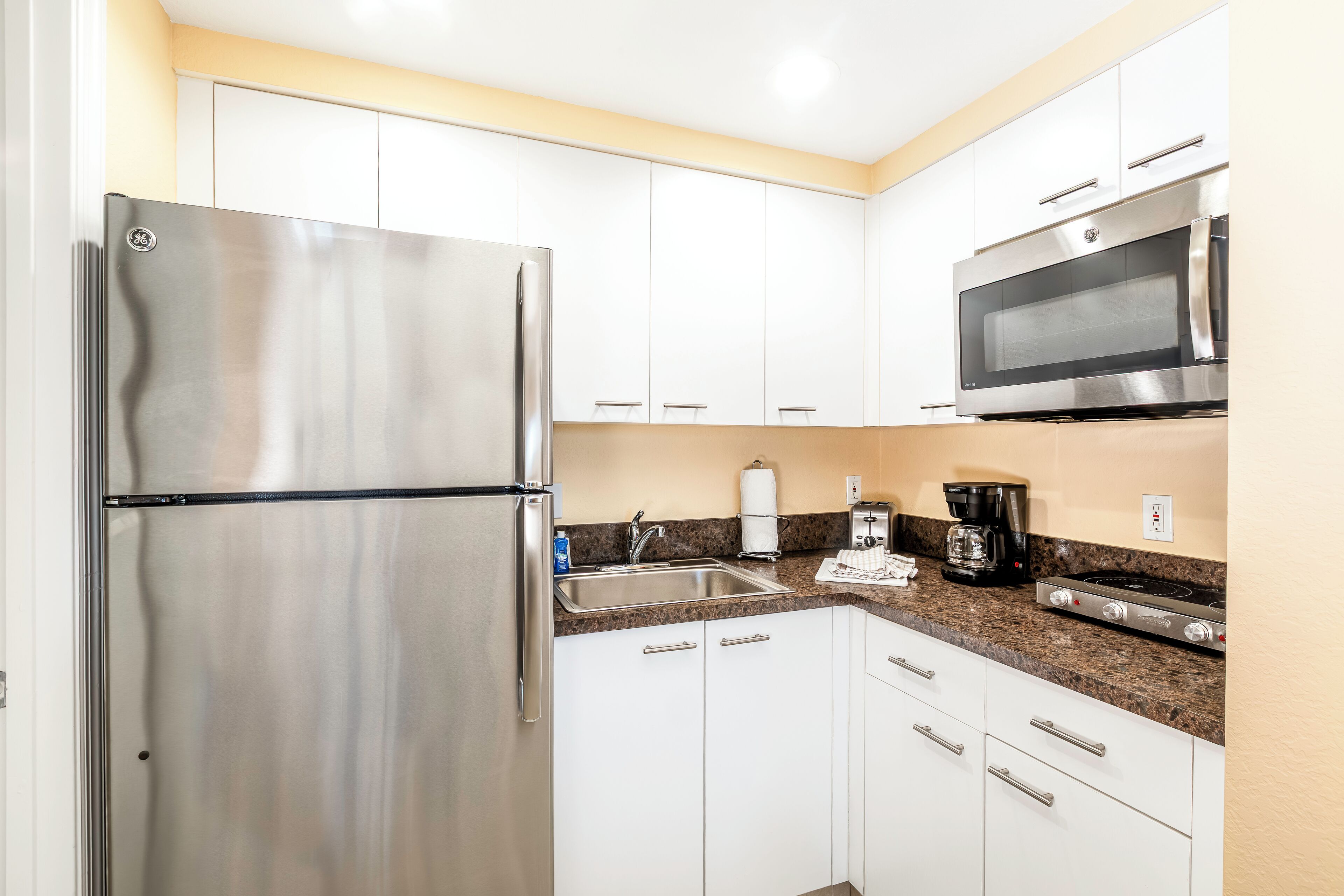 A modern kitchen with stainless steel appliances, white cabinets, granite countertops, and a built-in microwave.