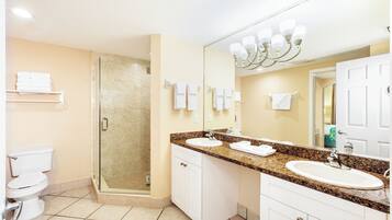 Un baño con cabina de ducha de vidrio, un lavabo con tocador y un espejo grande.