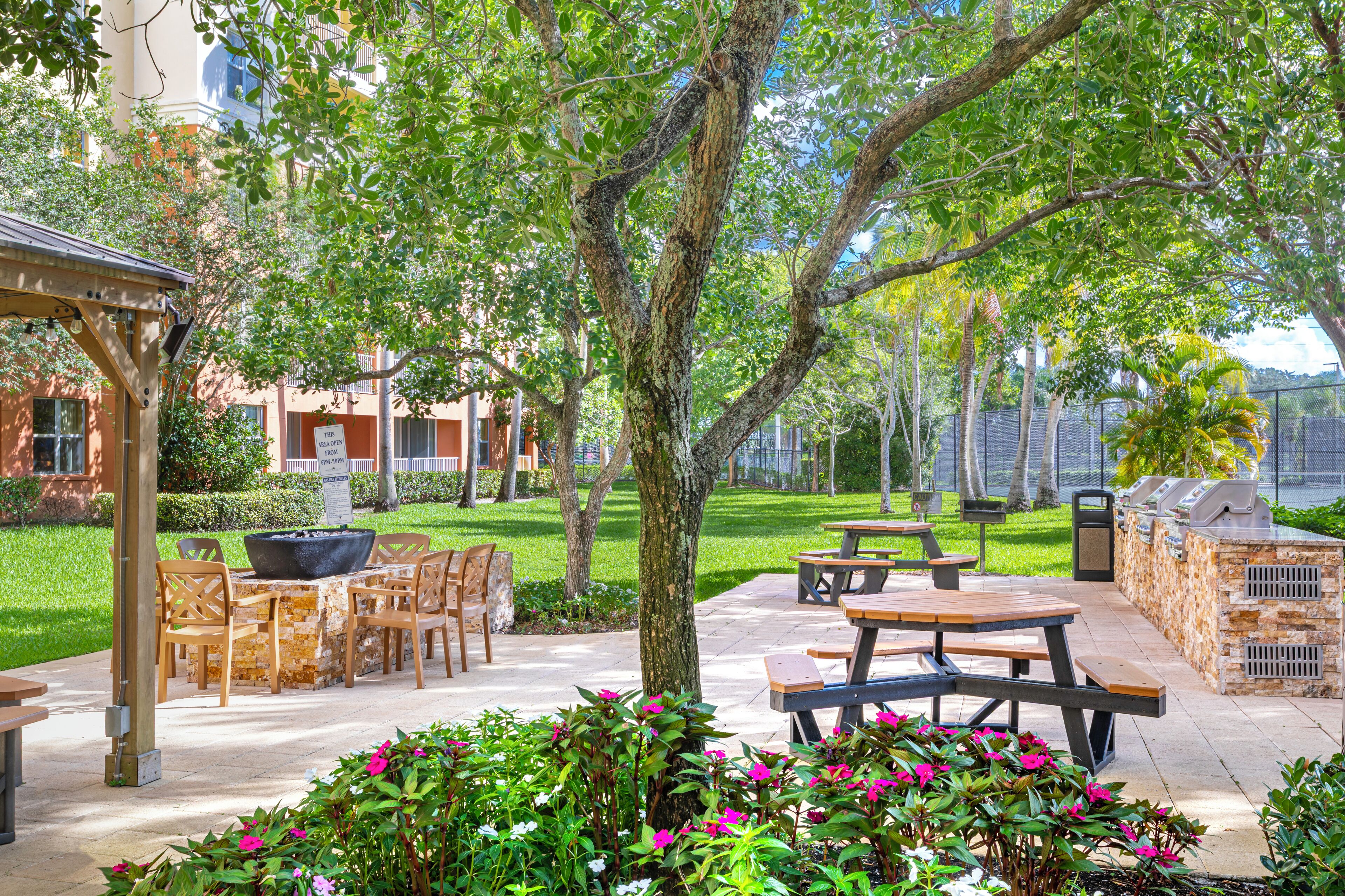 An outdoor patio area with picnic tables, a barbecue grill, and a stone barbecue station.