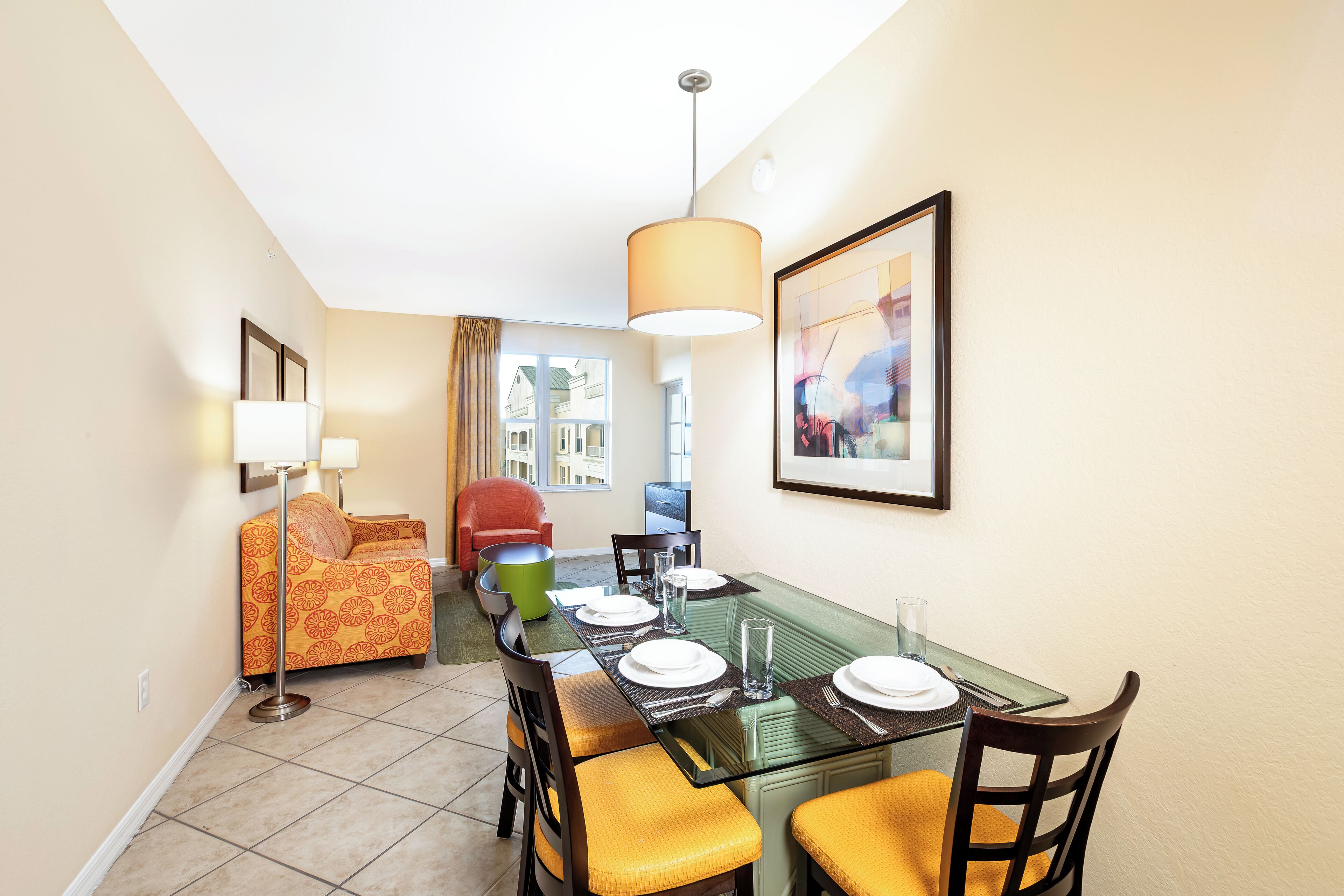 A dining area with a glass table, chairs, and a hanging lamp.
