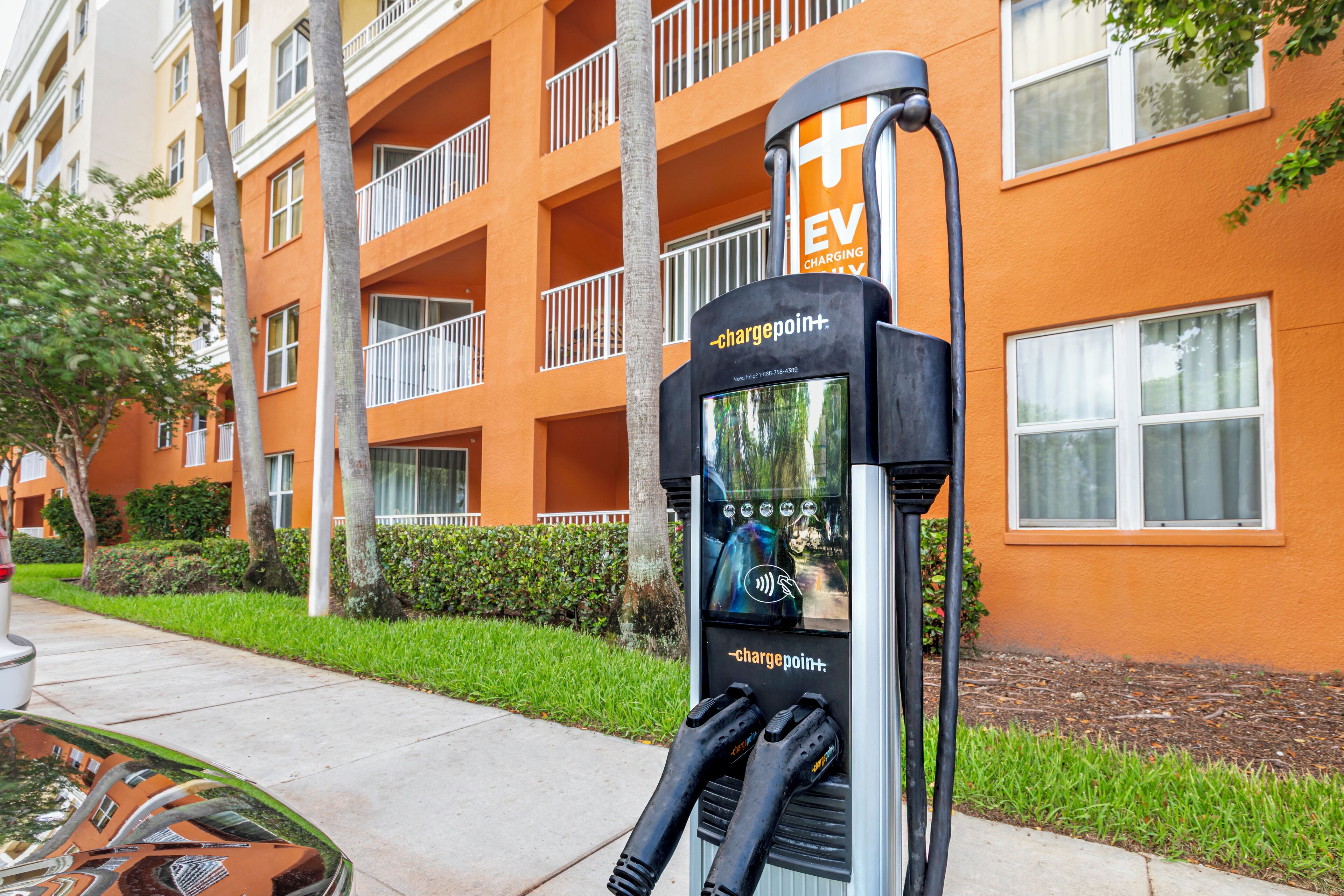 Une borne de recharge pour véhicules électriques se trouve devant un immeuble orange doté de balcons.