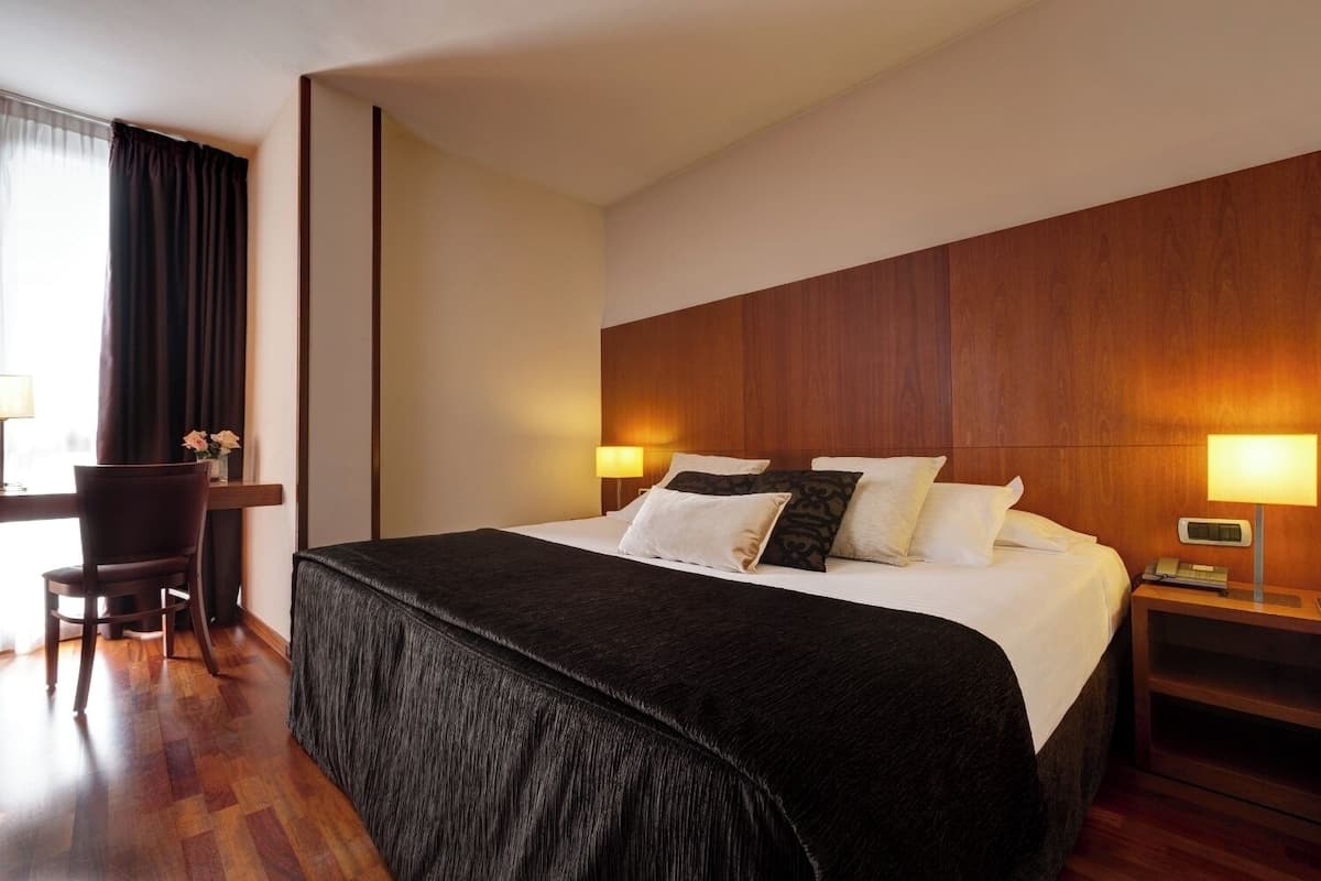 A hotel room with a large bed, a desk, and a chair.