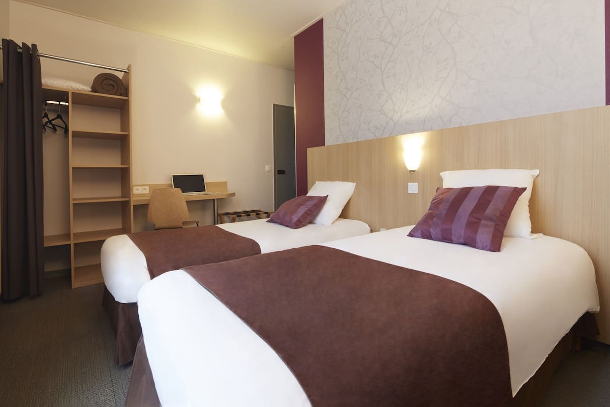 A hotel room with two beds, a desk, and a wardrobe.