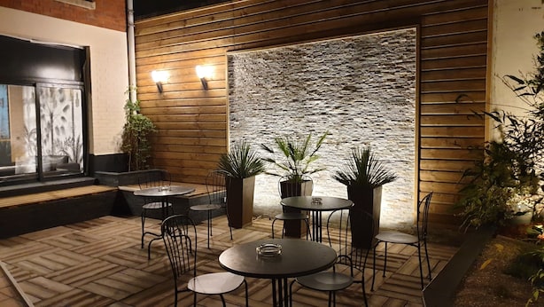 Une terrasse extérieure avec un sol en bois, des tables et des chaises en métal, et des plantes en pot.