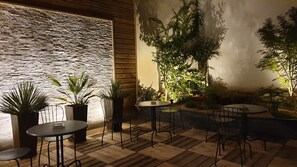 An outdoor seating area with tables and chairs, surrounded by potted plants and a stone wall. - Hotel Paris Villette (Paris)