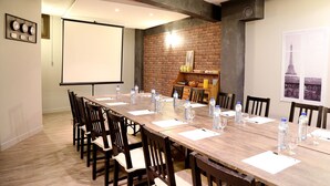 Une salle de conférence avec une longue table en bois, des chaises, des bouteilles d’eau et un écran de projection.