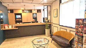 A reception area with a wooden counter, a television, a potted plant, a sofa, and a glass coffee table. - Hotel Paris Villette (Paris)