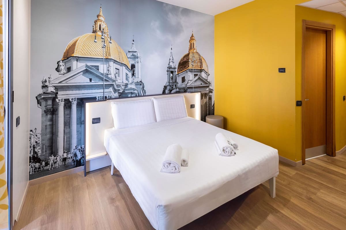 A hotel room with a large bed, a mural of historical buildings, and a wooden floor.