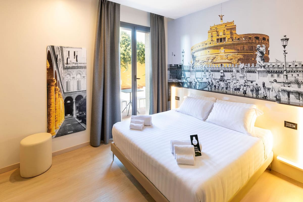 A hotel room with a large bed, a small round table, and a window with curtains.