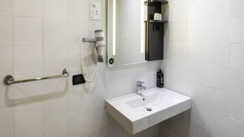A bathroom with a white sink, a mirror, a hairdryer, and a shelf with toiletries.
