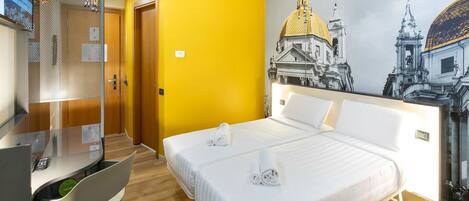 A hotel room with a bed, a desk, and a chair. There is a painting of a building on the wall.