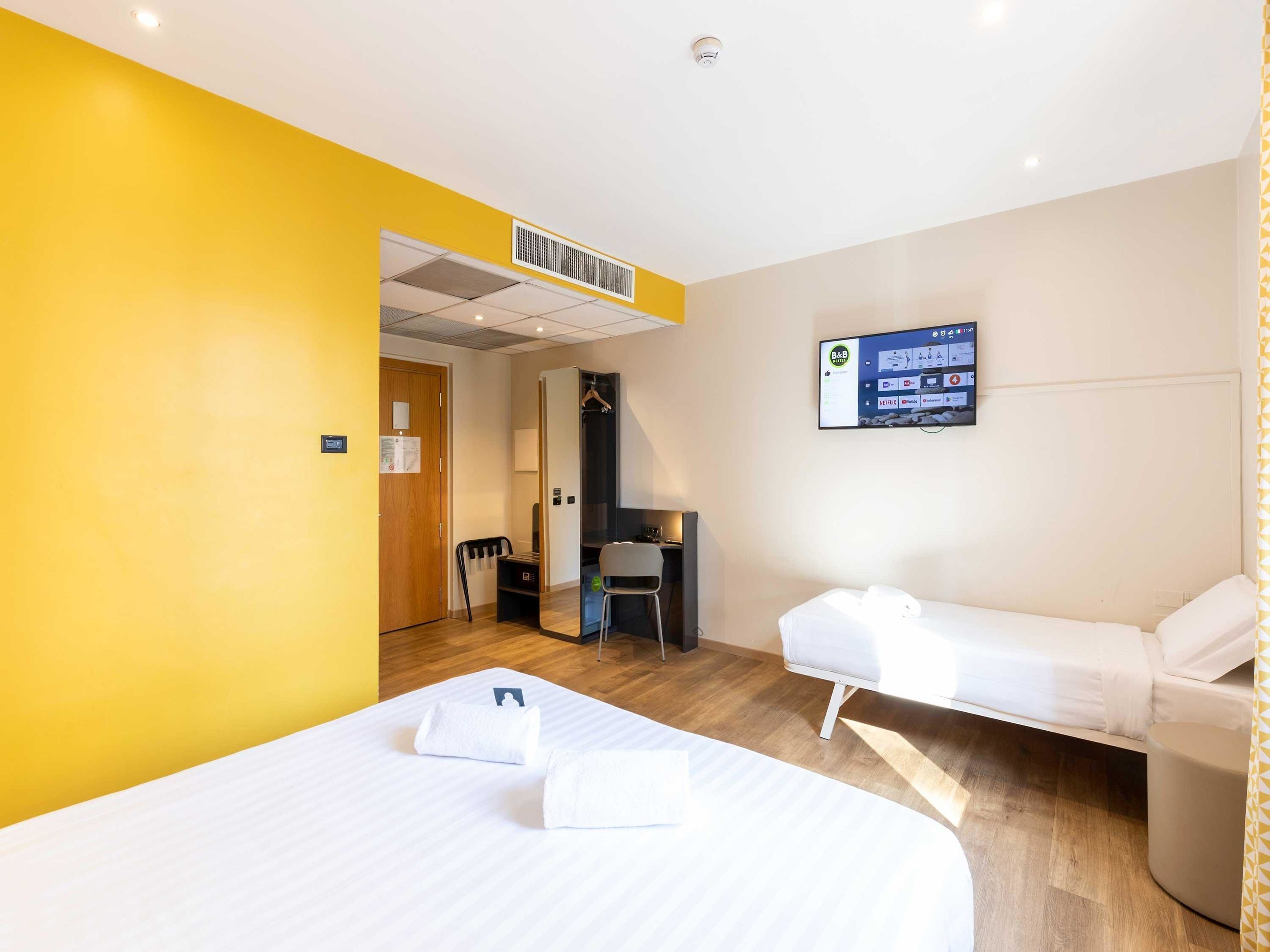 Une chambre d’hôtel avec deux lits, un téléviseur fixé au mur et un plancher en bois.