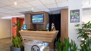 Un mostrador de recepción con el logotipo de B&B, una pantalla digital y plantas en macetas.