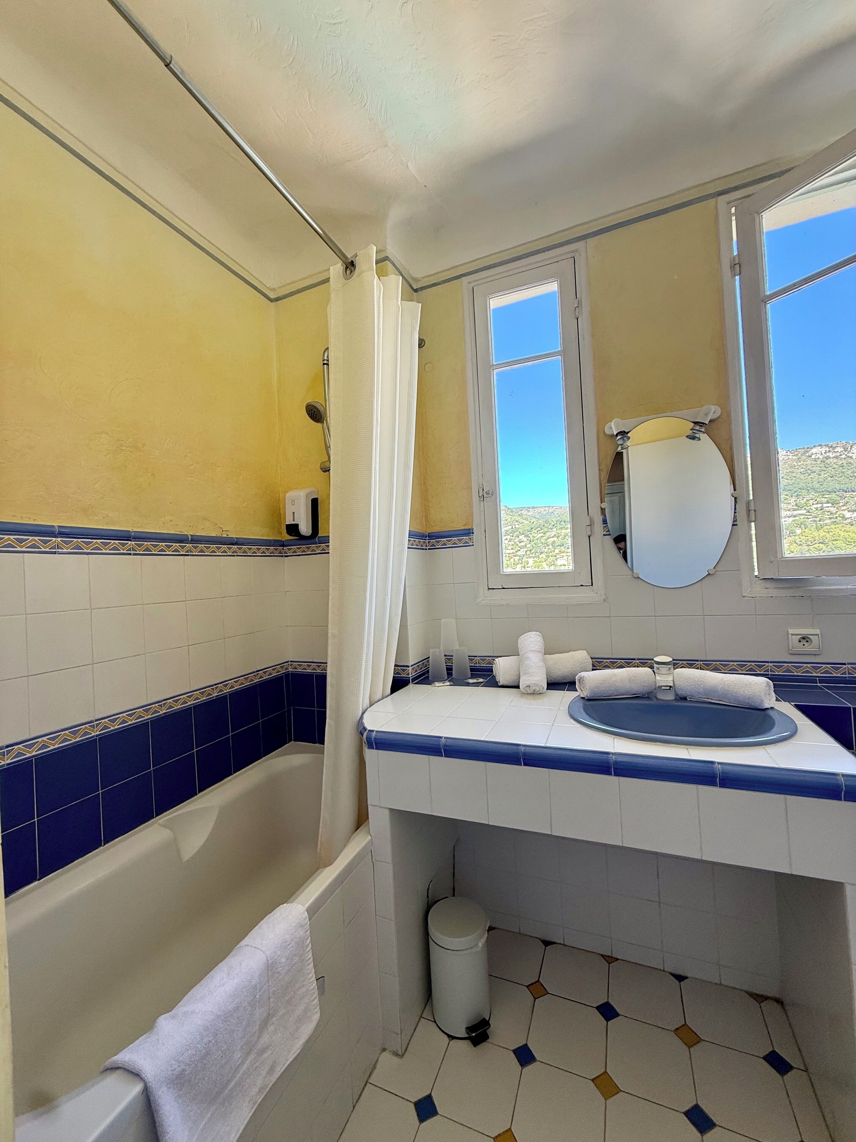 A bathroom with a bathtub, a sink, a mirror, and a window with a view of a landscape.