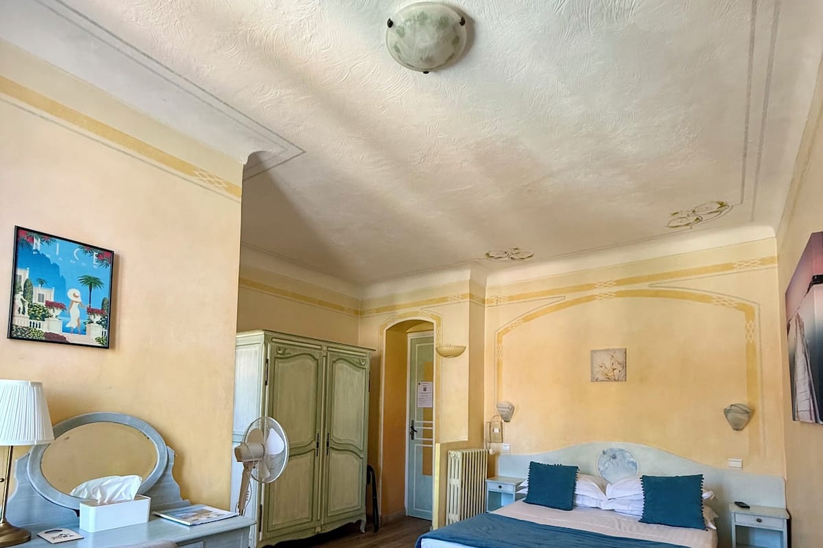 A hotel room with two beds, a desk with a chair, a mirror, a radiator, and a painting on the wall.