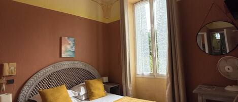 A hotel room with a bed, a desk, a chair, a bedside table, a telephone, and a window with curtains.