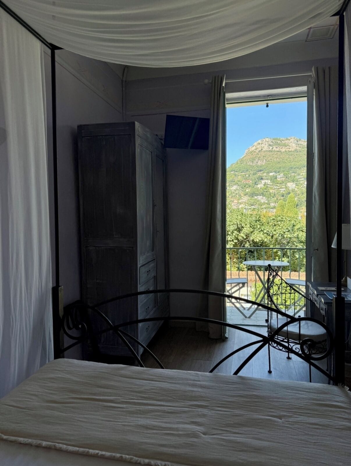 A bedroom with a bed, a wardrobe, a small table, and a view of a mountainous landscape through a window.