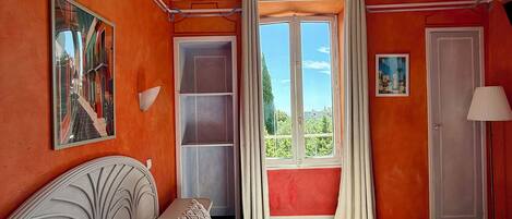 A hotel room with a bed, a sofa, a window with curtains, a door, and a painting on the wall.
