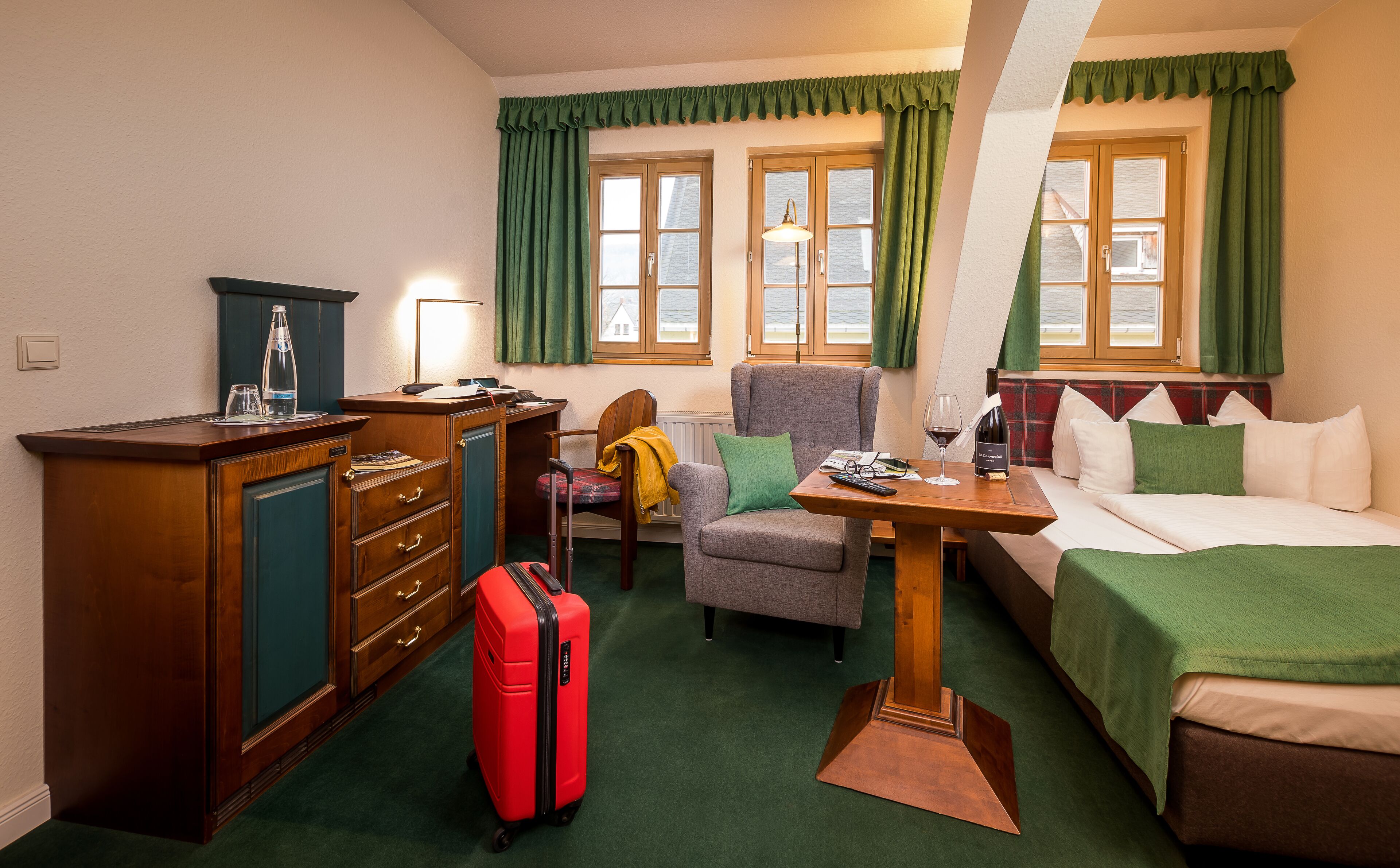 Una habitación de hotel con escritorio, silla, cama y una maleta roja.