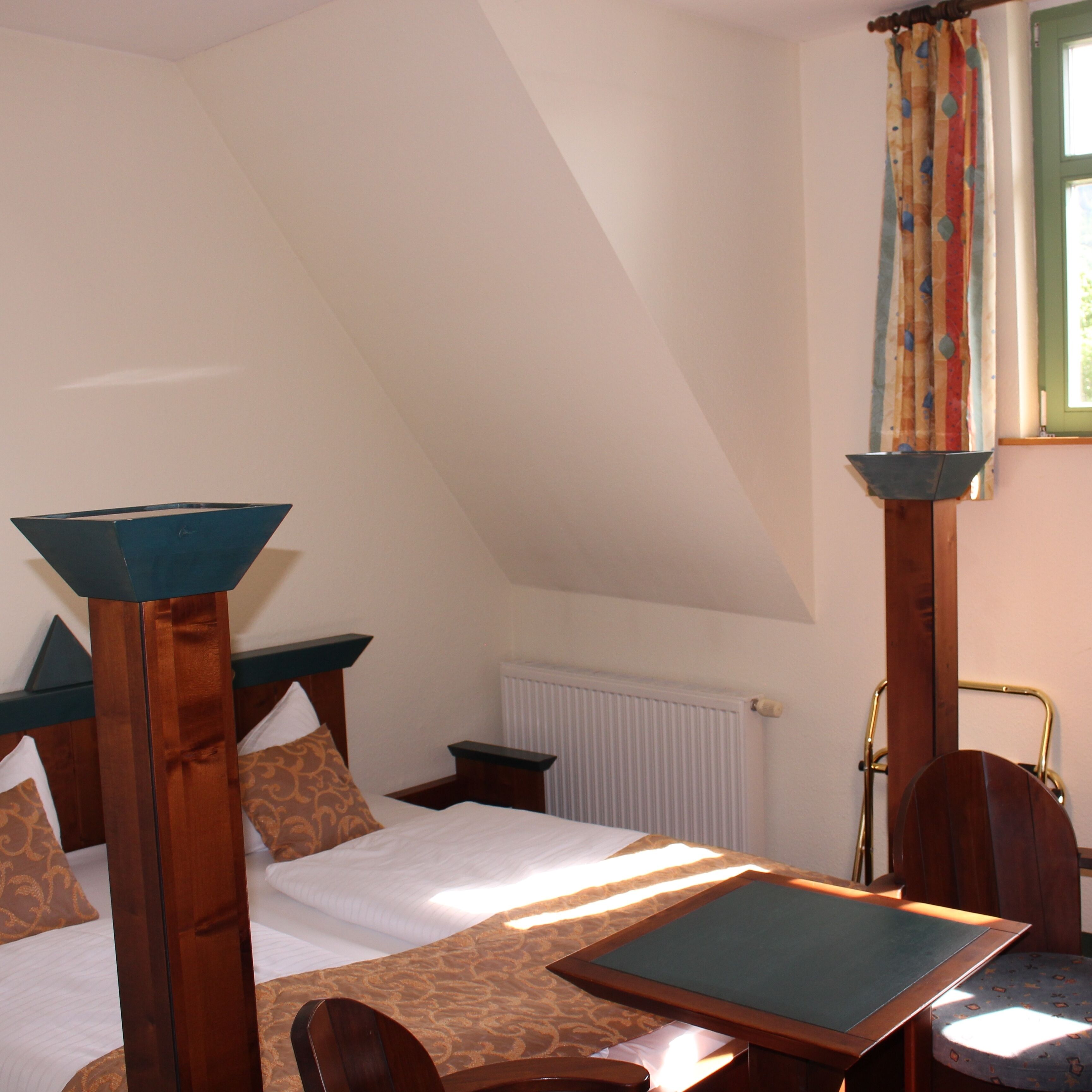 A bedroom with a sloped ceiling, a bed with a wooden headboard, a table, and a chair.