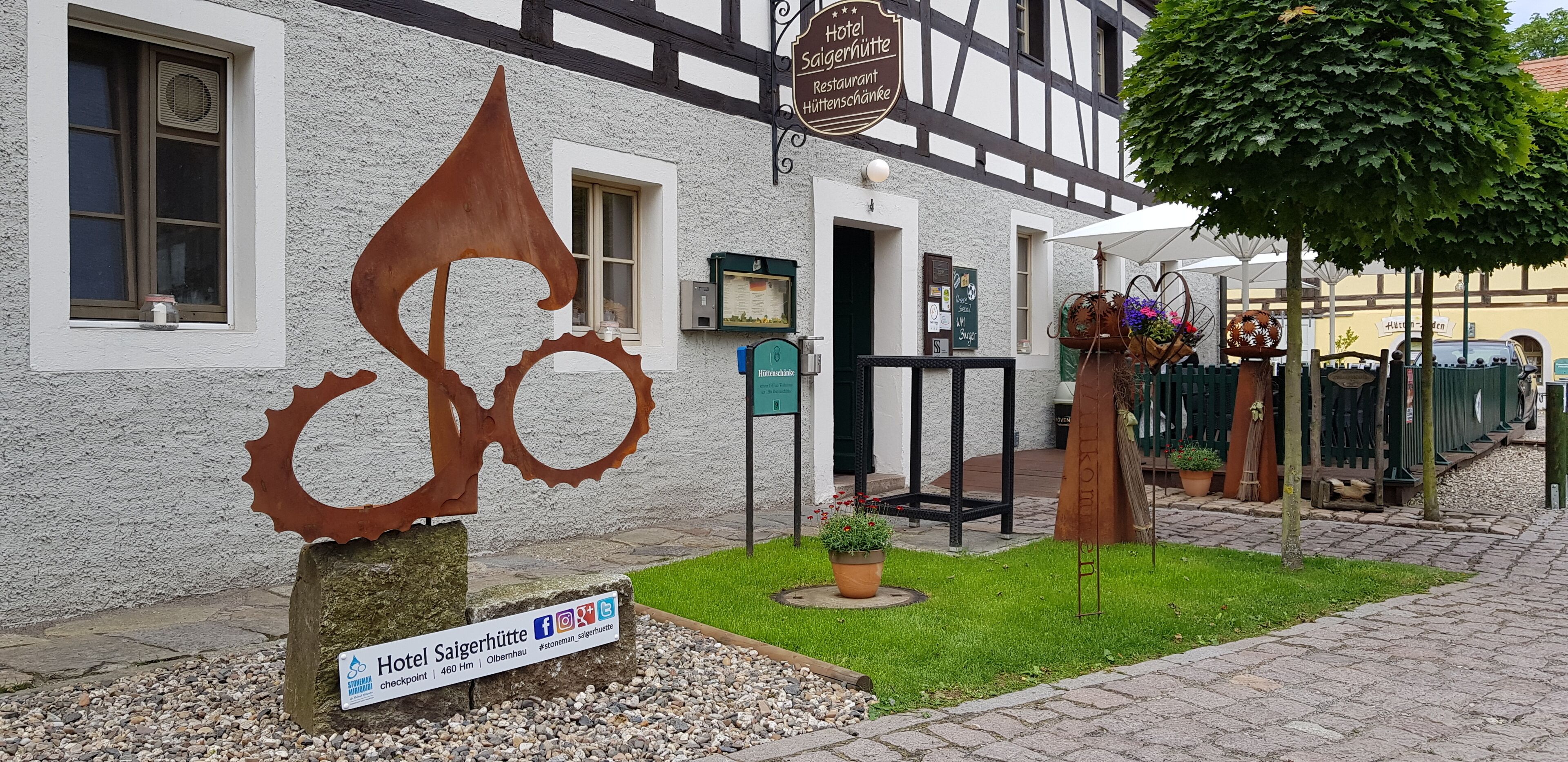 Un hotel que muestra un cartel indicando que es restaurante y jardín de cerveza. Frente al edificio hay una escultura metálica de una bicicleta.