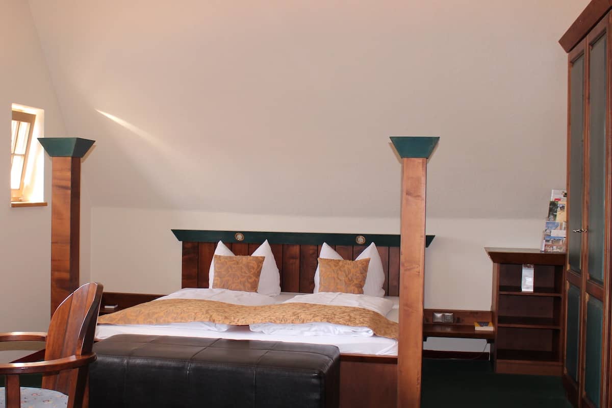 A four-poster bed with a wooden headboard, a wooden nightstand, a chair, and a wardrobe.