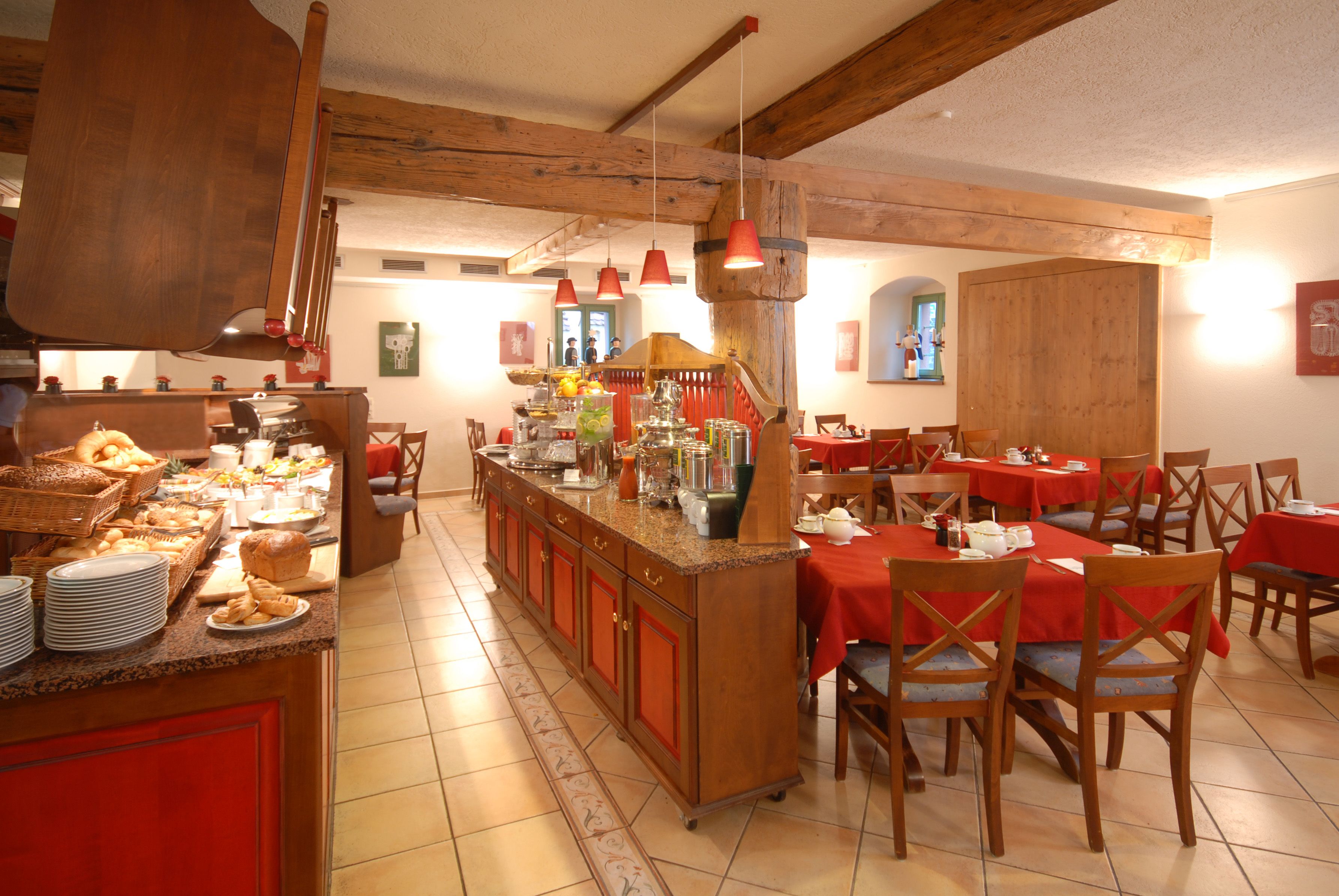 Un restaurante con barra central, varias mesas con manteles rojos y sillas de madera.