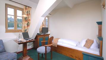 Una habitación pequeña y acogedora con una cama, un escritorio con una computadora portátil, una silla y una ventana con cortinas.