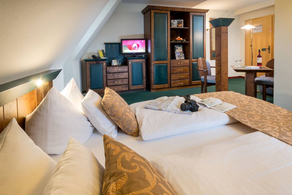 A hotel room with a bed, pillows, a television, a desk with a chair, and a wooden cabinet.