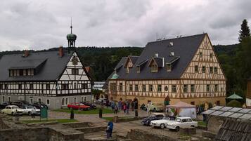 Ein traditionelles Fachwerkhäuschen mit einem Glockenturm, umgeben von geparkten Oldtimern und einer Kopfsteinpflasterstraße.