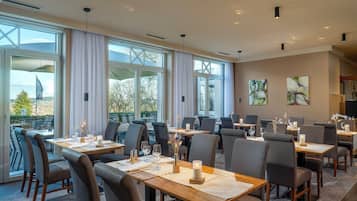 A restaurant with multiple tables and chairs, large windows, and artwork on the walls.