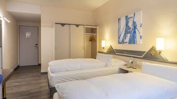 A hotel room with two beds, a wardrobe, a bedside table with a lamp, and a painting on the wall.