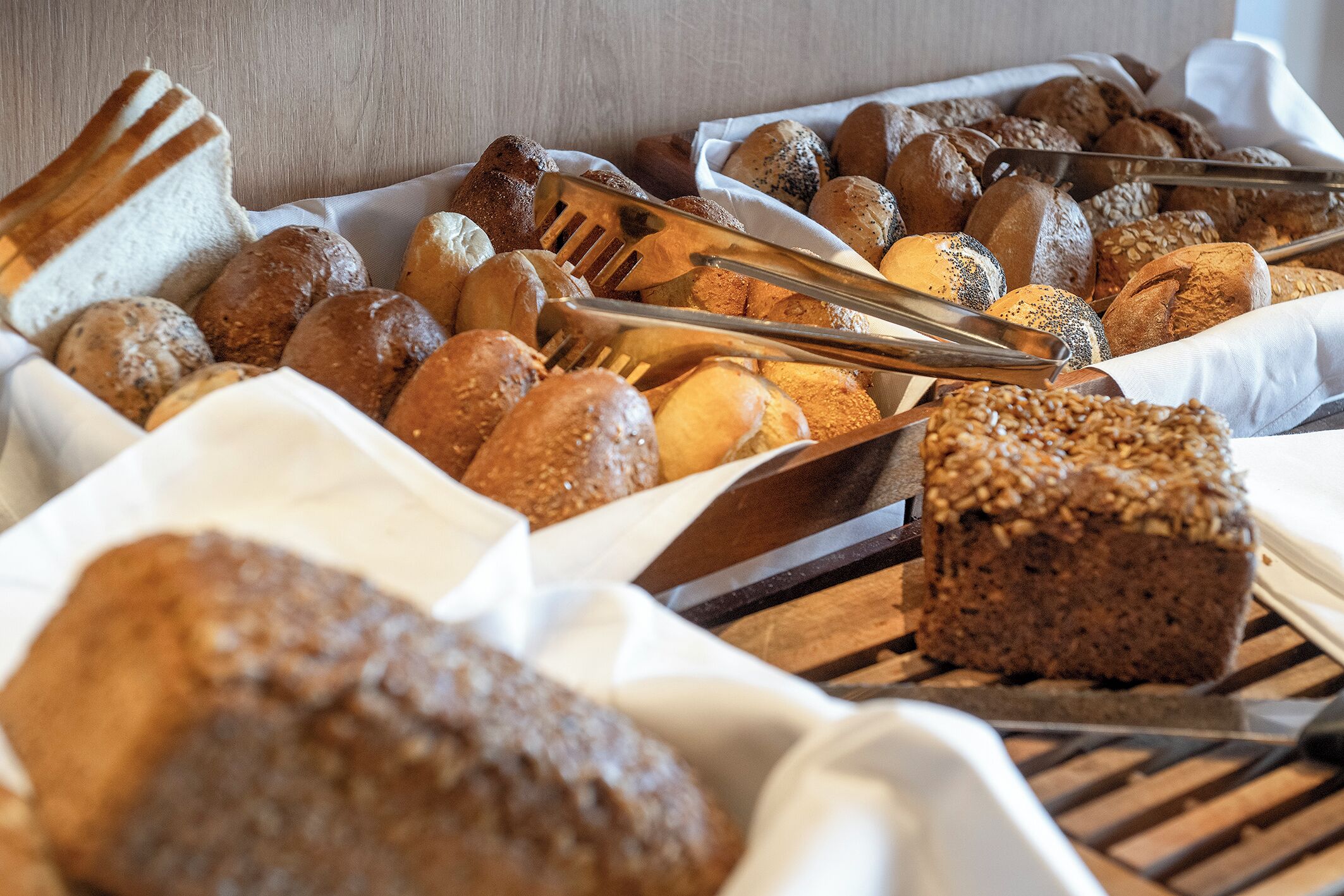 A variety of breads and pastries displayed on a wooden rack with tongs.