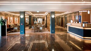 A spacious lobby with a reception desk, seating area, and a well-lit corridor. - Parkhotel Berghoelzchen (Hildesheim)