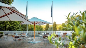 An outdoor patio with tables and chairs, umbrellas, and a white fence. - Parkhotel Berghoelzchen (Hildesheim)