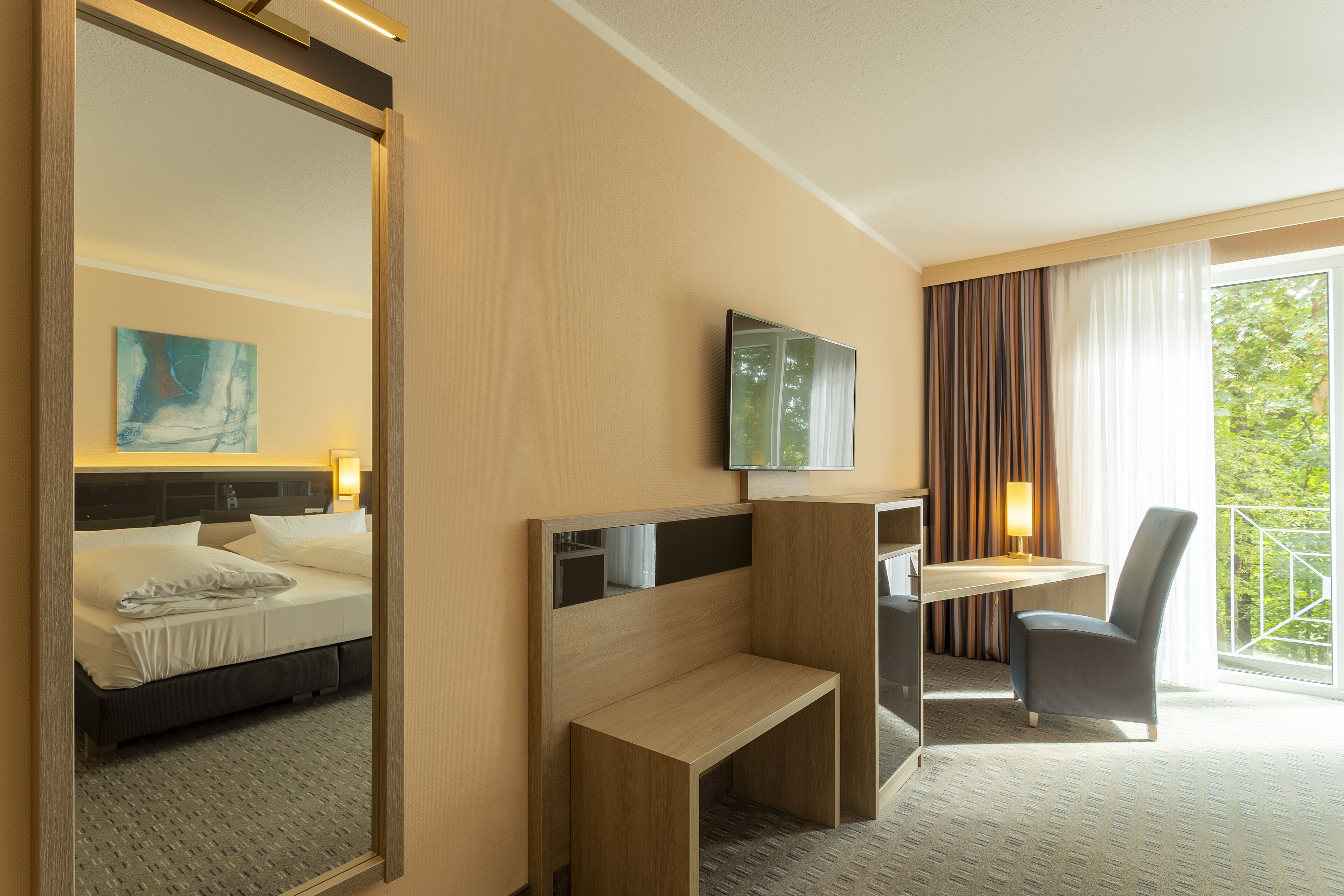 A hotel room with a bed, a desk, a chair, a TV, and a window with curtains.