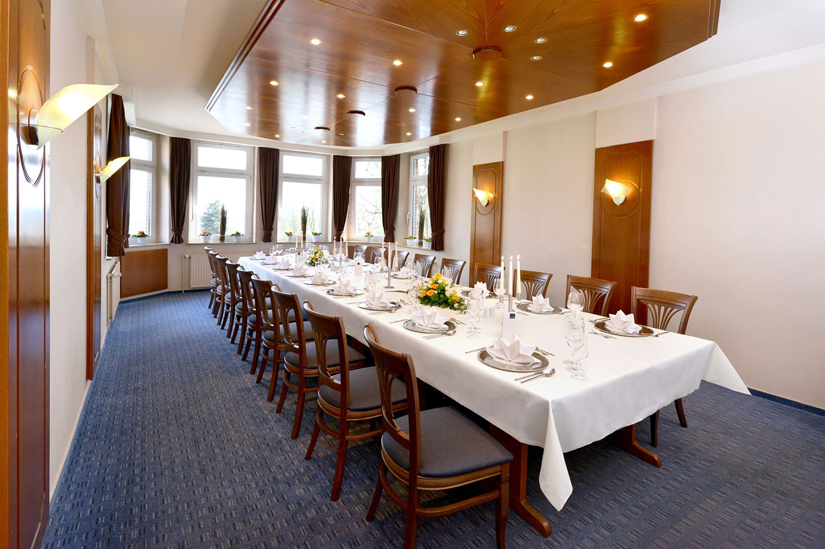 A long dining table set for a formal meal with chairs, candles, and a blue carpeted floor.