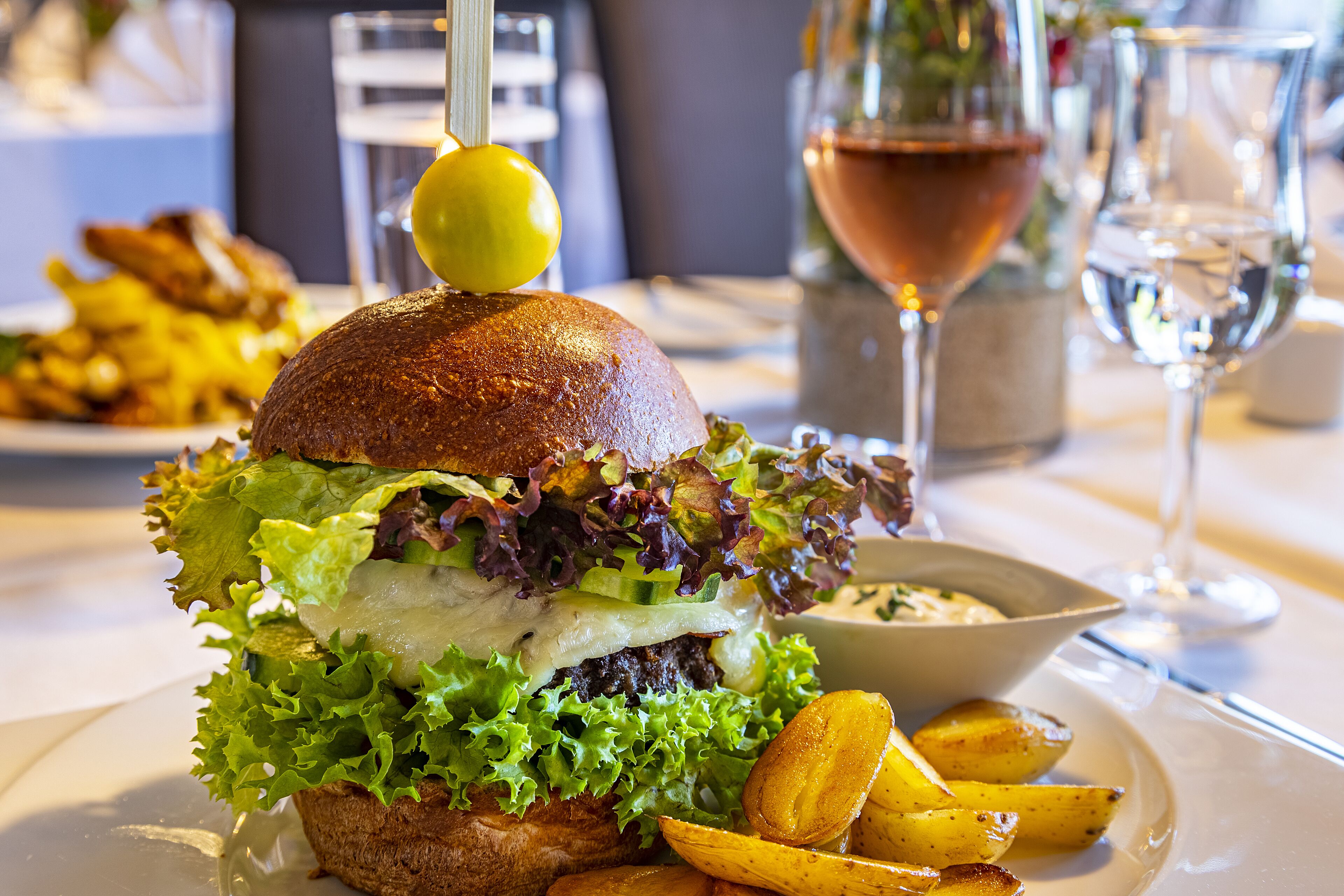 Ein Burger mit Zitrone, dazu Pommes und ein Glas Wein auf einem Tisch.