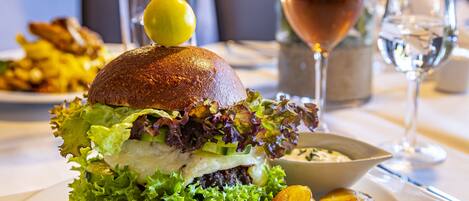 Un hamburger con un limone sopra, accompagnato da patatine fritte e un bicchiere di vino su un tavolo.