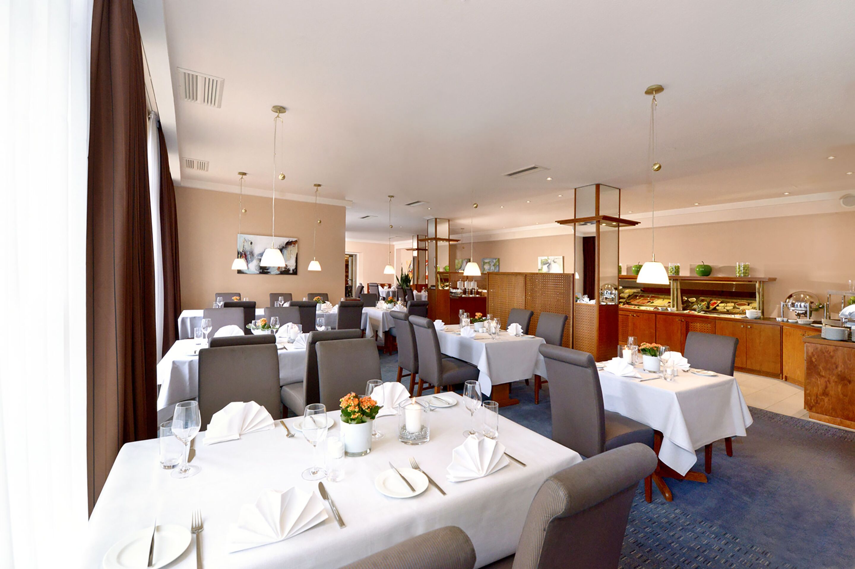 Ein Hotel-Speisesaal mit mehreren gedeckten Tischen, einem Buffetbereich und Blick auf die Stadt durch große Fenster.