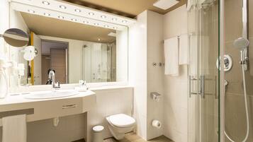 A modern bathroom with a large mirror, a sink, a toilet, and a glass-enclosed shower area.