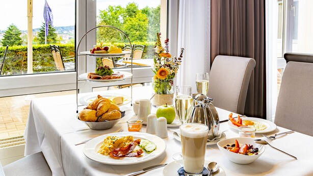 A breakfast table with a variety of dishes, including eggs, bacon, and fruit, and a vase of flowers. - Parkhotel Berghoelzchen (Hildesheim)