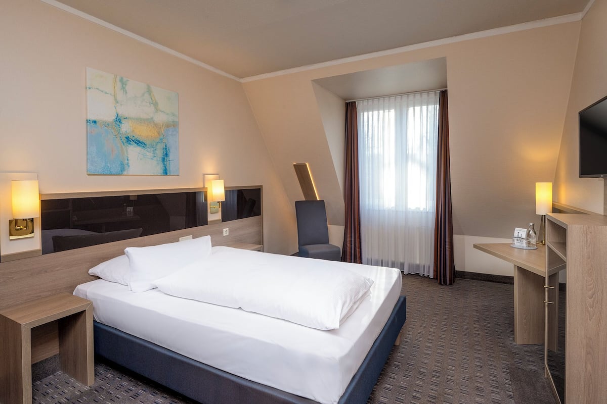 Ein Hotelzimmer mit Bett, Schreibtisch, Stuhl, Fernseher und Bildern an der Wand.