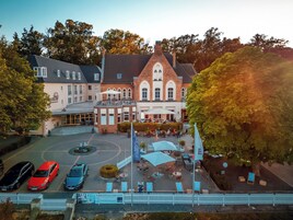 Un hotel con patio central, mobiliario exterior y un estacionamiento con varios vehículos.