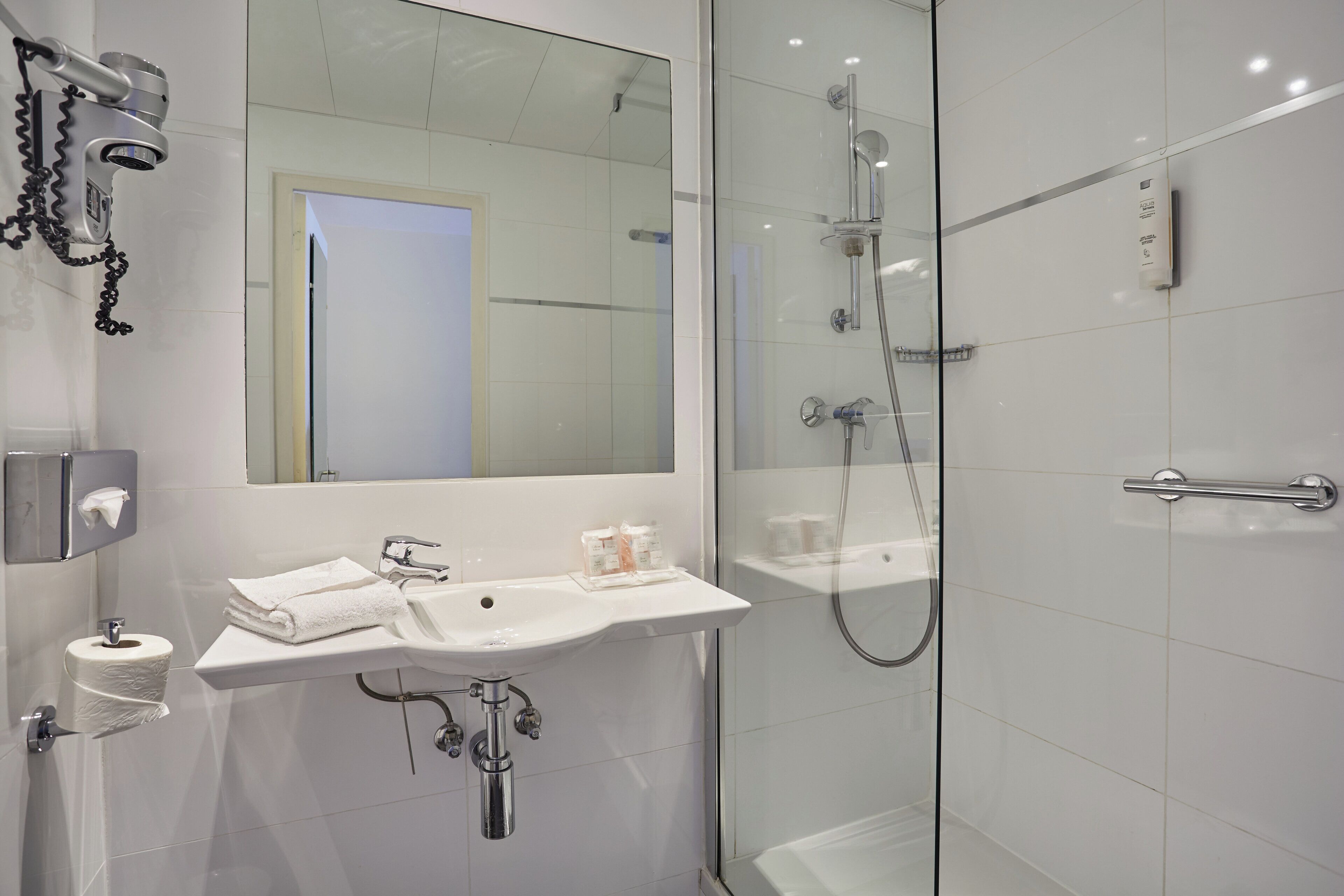 A modern bathroom with a glass shower enclosure, a white sink with a mirror above it, and a towel dispenser.
