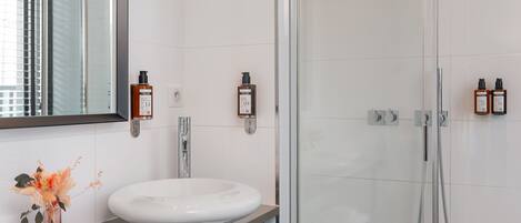 A modern bathroom with a glass-enclosed shower, a white sink, and a mirror above it.