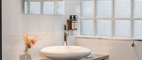 A modern bathroom with a large mirror, a white sink, and a window with frosted glass.