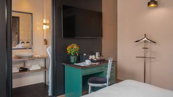 Una habitación de hotel moderna con cama, escritorio con silla, televisor y baño con lavamanos y espejo.