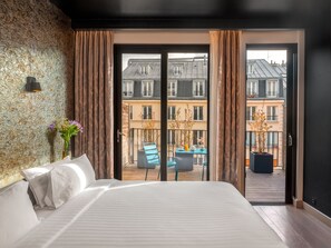 A bedroom with a large bed, a view of a balcony with outdoor furniture, and a textured wall. - Grand Hotel Lafayette (Paris)