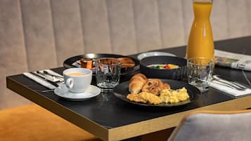 A breakfast table with croissants, scrambled eggs, and a glass of orange juice.